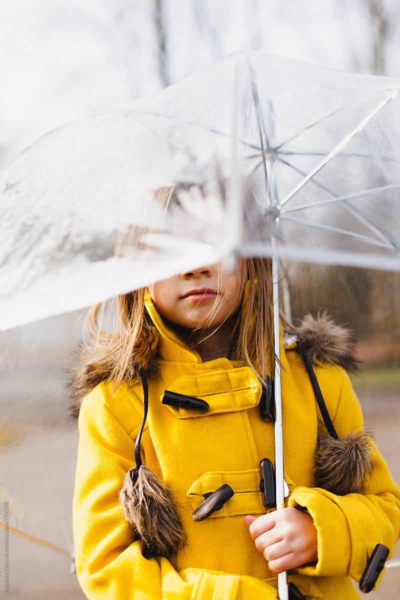 Girl wearing yellow gold duffle coat is holding a clear umbrella