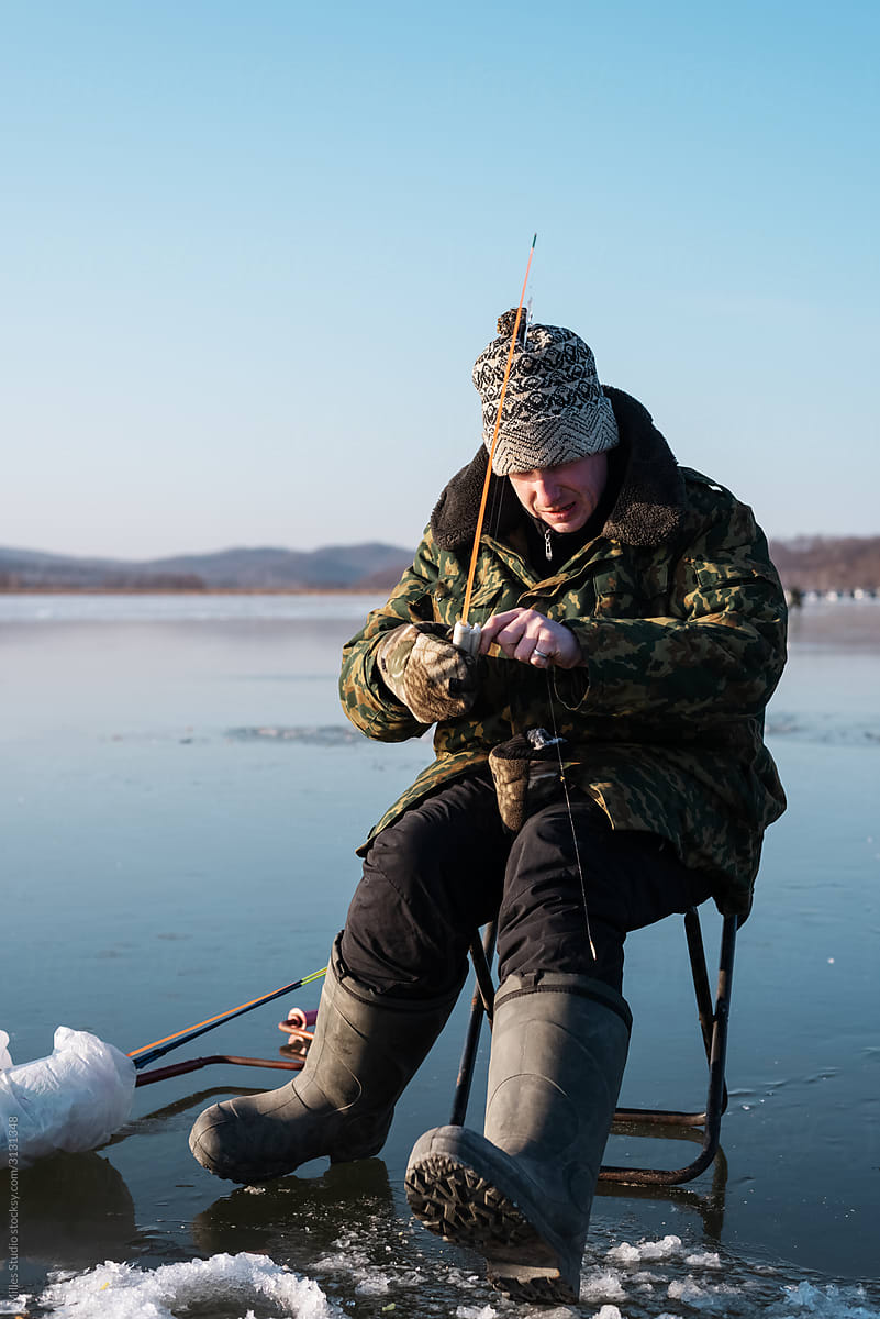 Fisherman reeling empty line on frozen reservoir