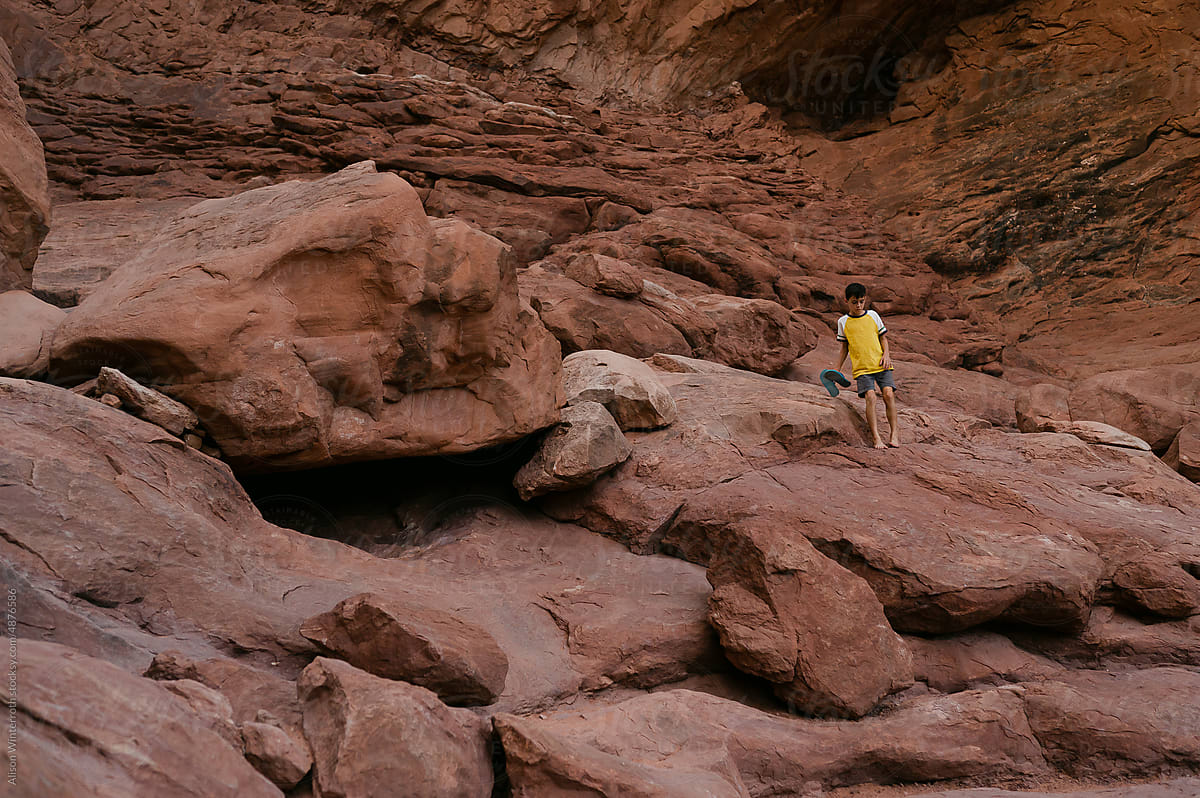 Wide angle image boy climbs down rocks barefoot