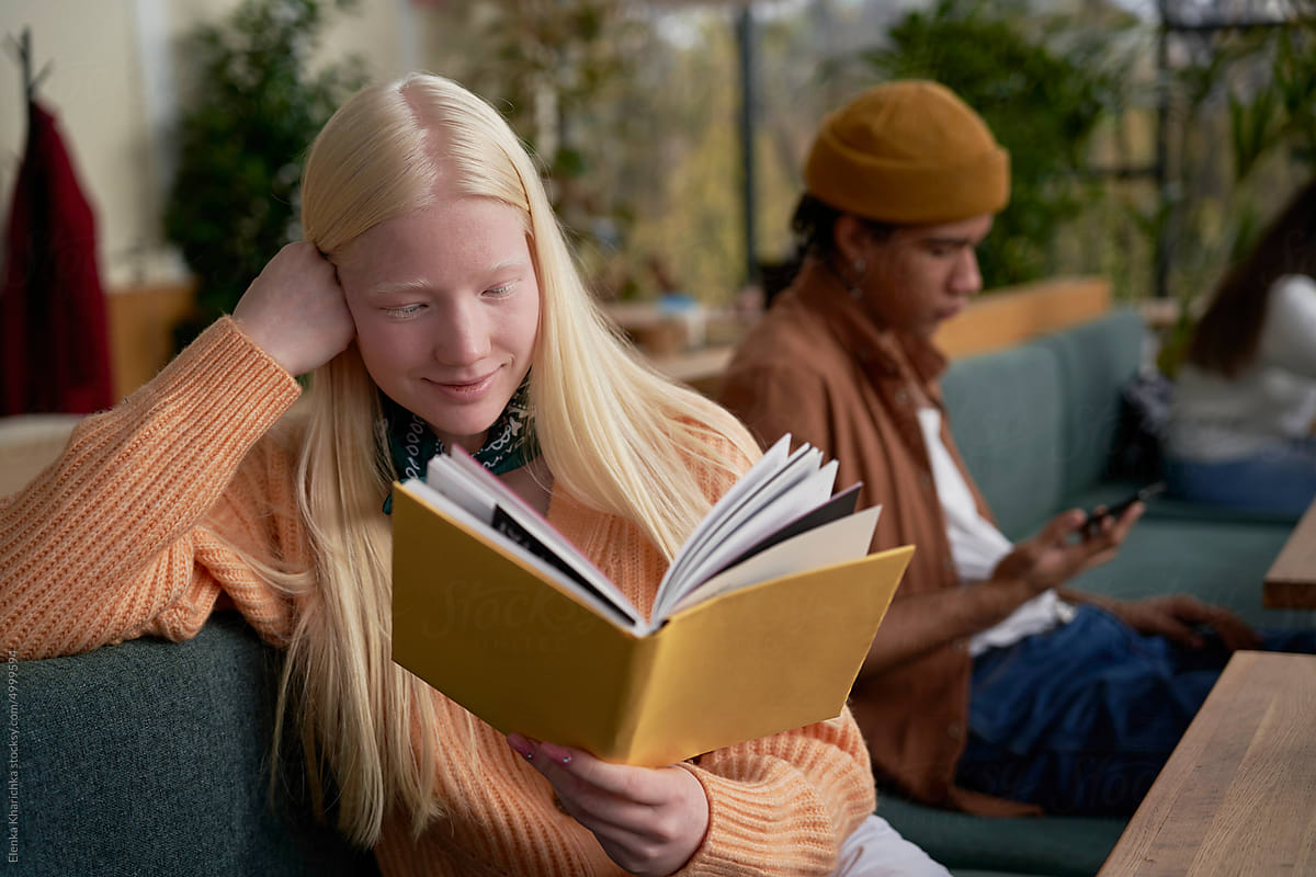 A cheerful albino woman reading a book in a café
