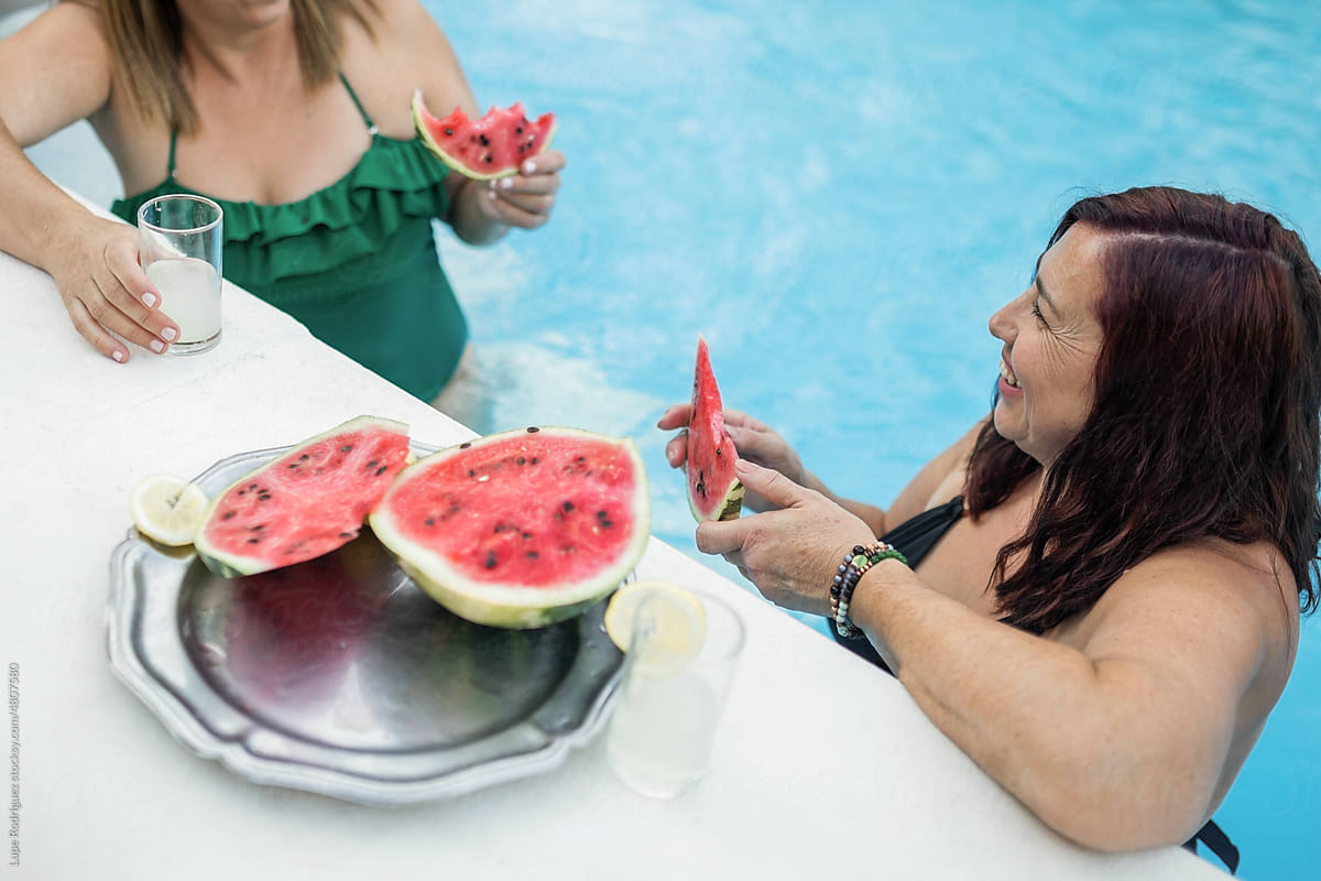 mature women inside a pool eating watermelon while talking