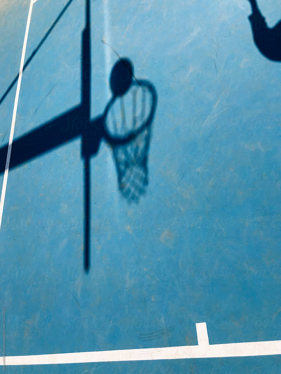 Silhouette of a basketball falling into basket on blue court.