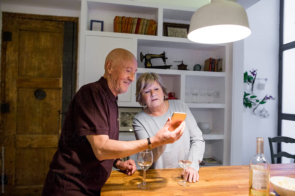 Elderly couple using their phone whilst drinking wine at home.