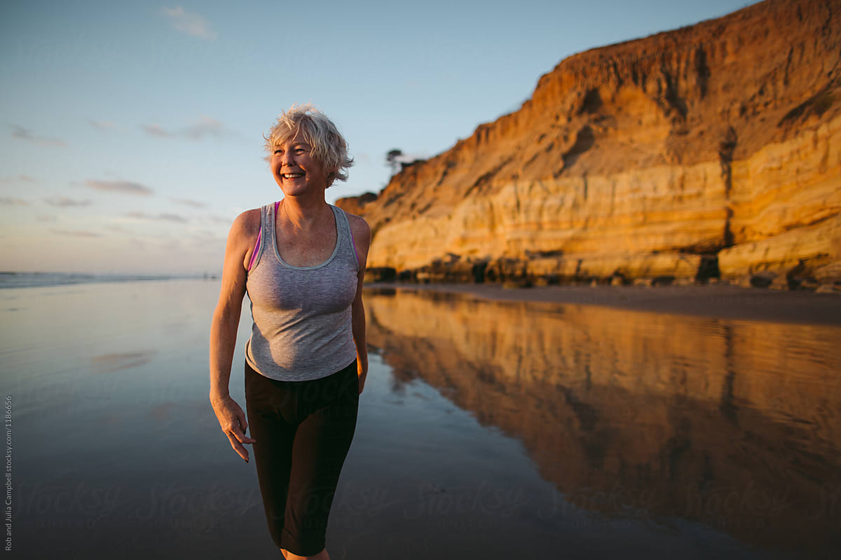 Vibrant Mature Woman Enjoying Herself On The Beach At Sunset Del Colaborador De Stocksy Rob 