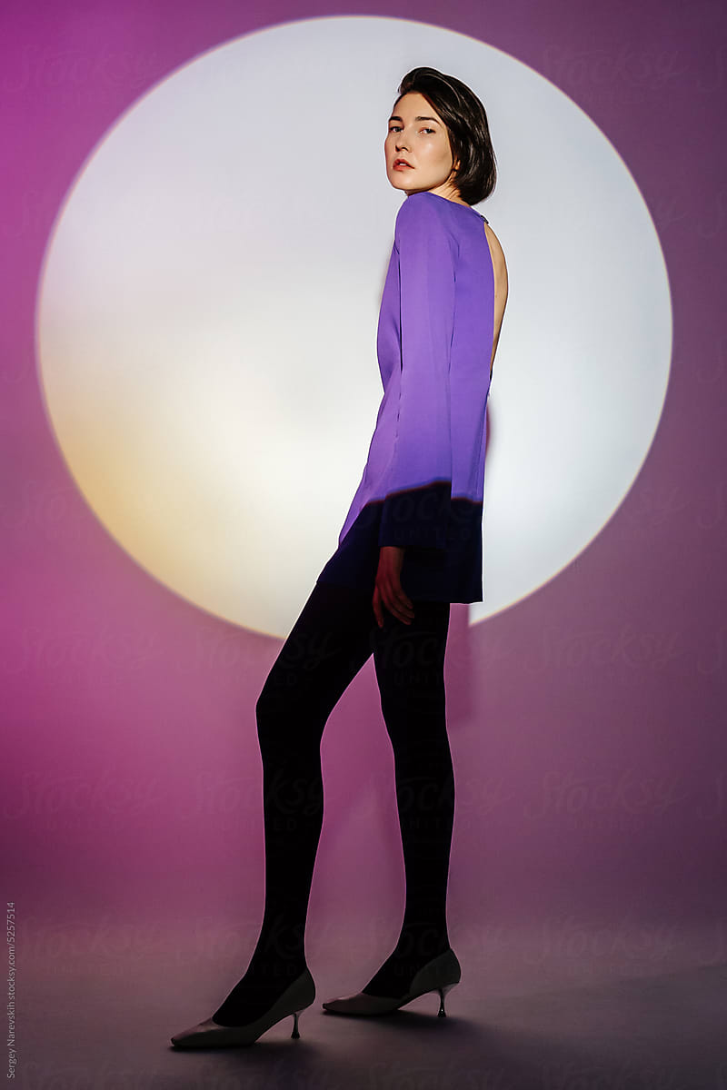 Stylish woman in purple dress against projector light