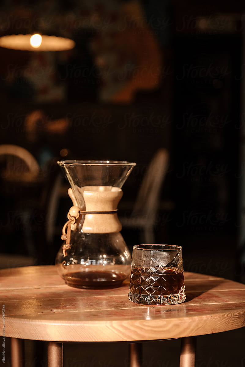 One glass with coffee on wooden table with chemex