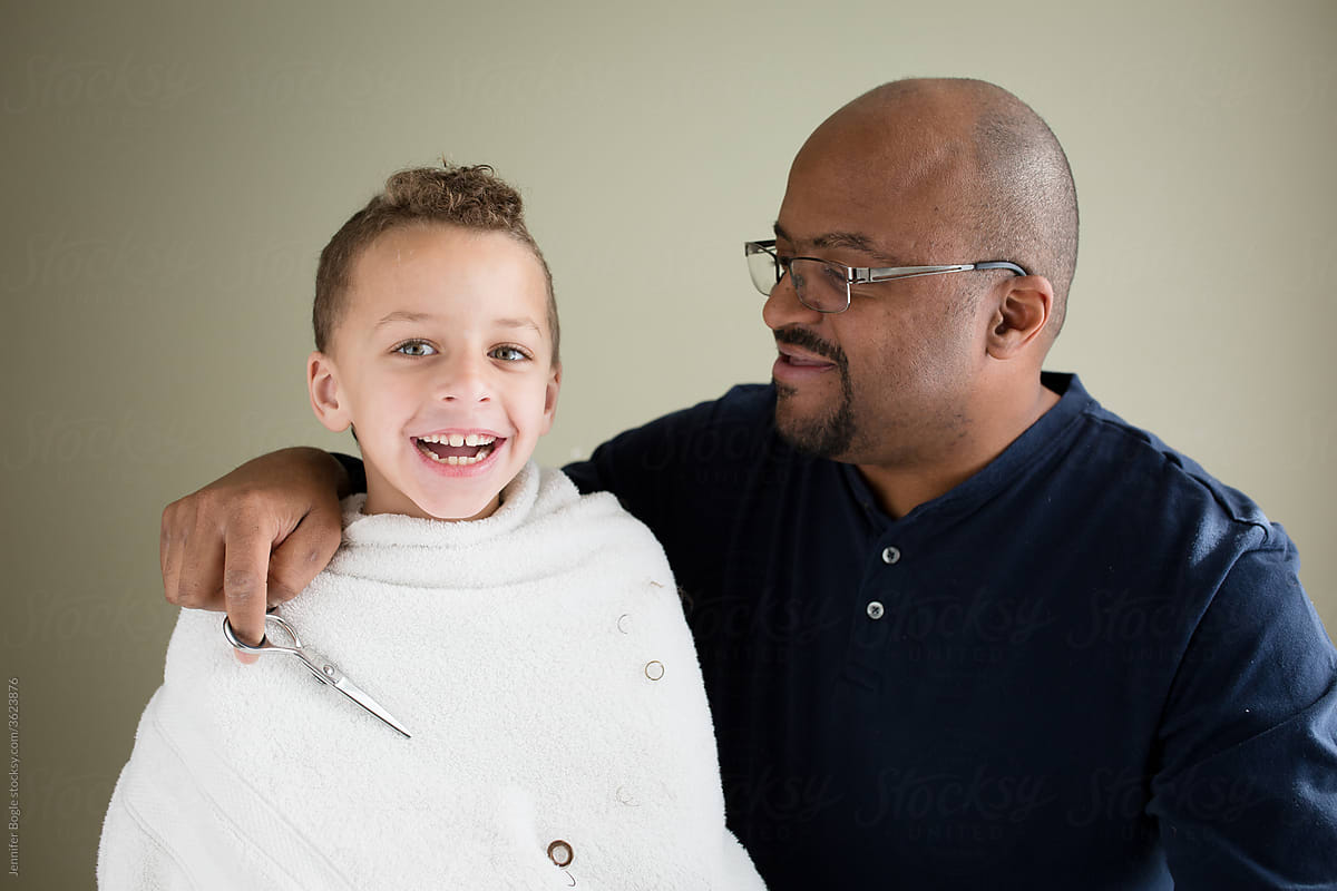 Dad with scissors hugs smilng son during home haircut