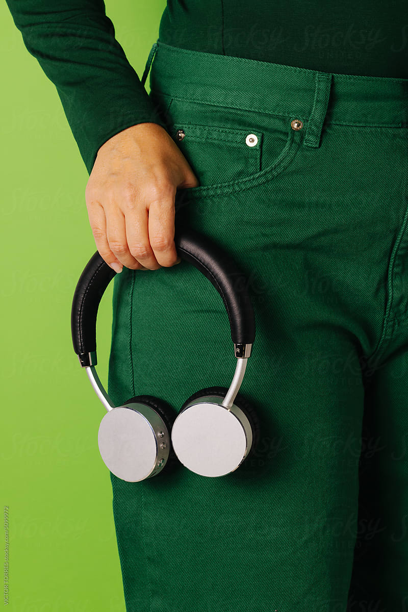 Crop person holding grey headphones over green background