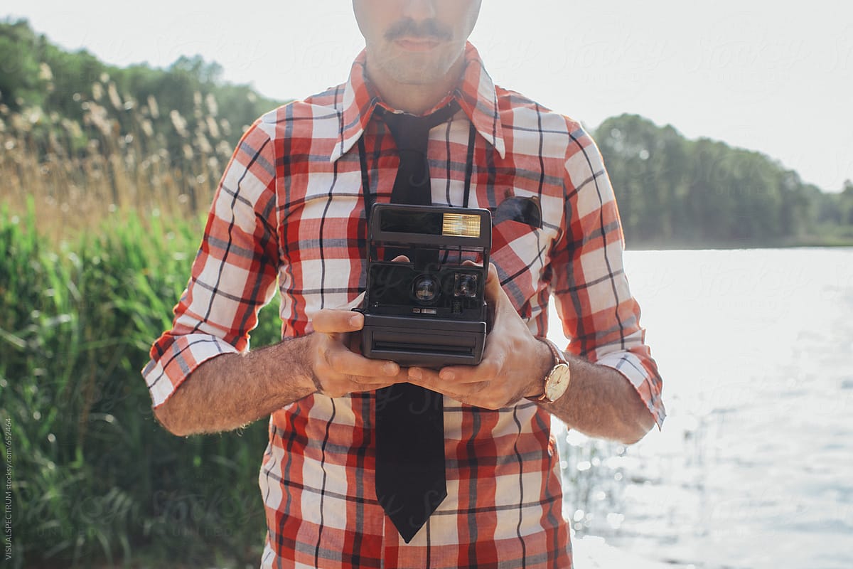 Retro-Styled Man With Moustache Holding Polaroid Camera in Front of Chest