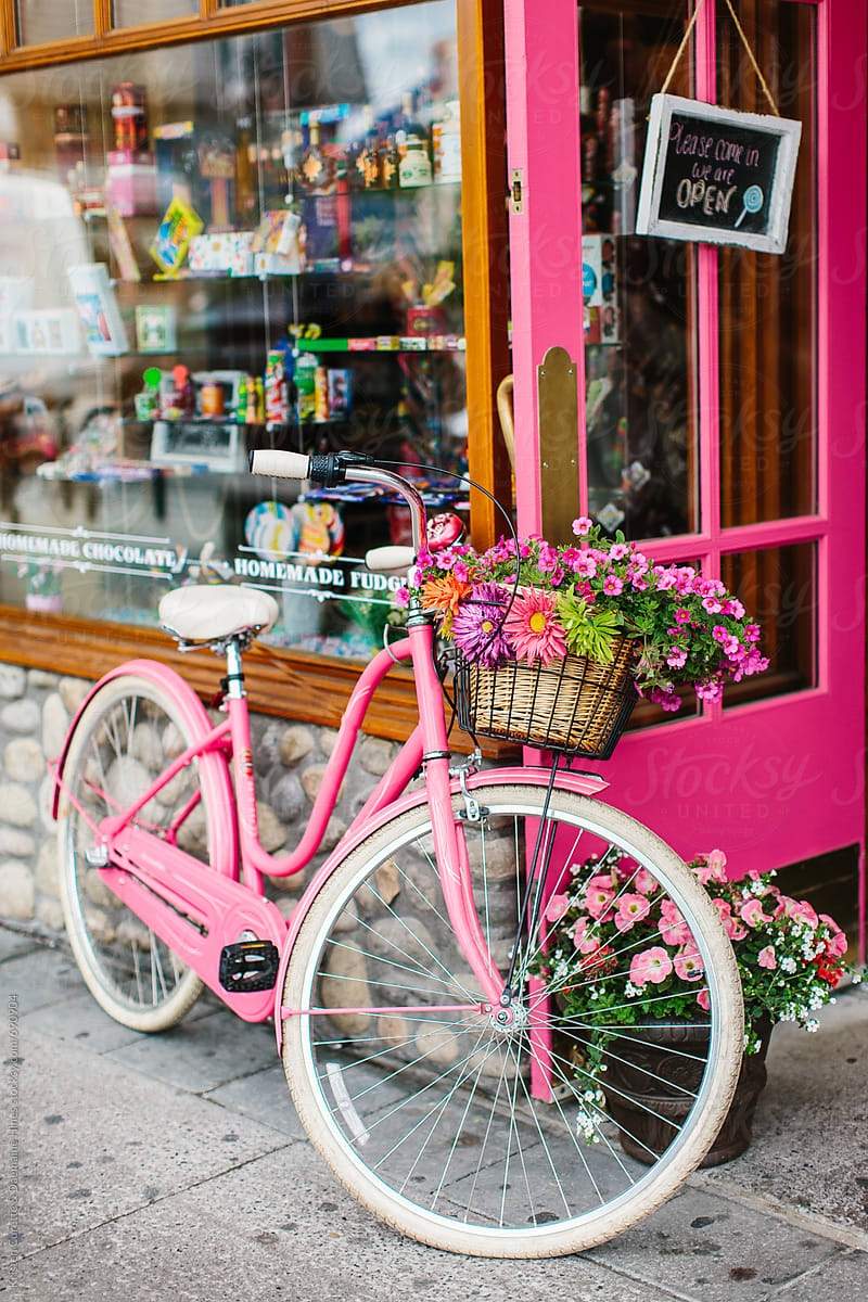 A pink cruiser bike with flowers infront of a candy store