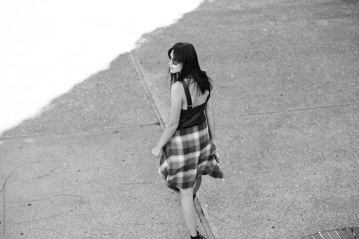 A woman walking away from camera on a street with a plaid shirt tied around her waist