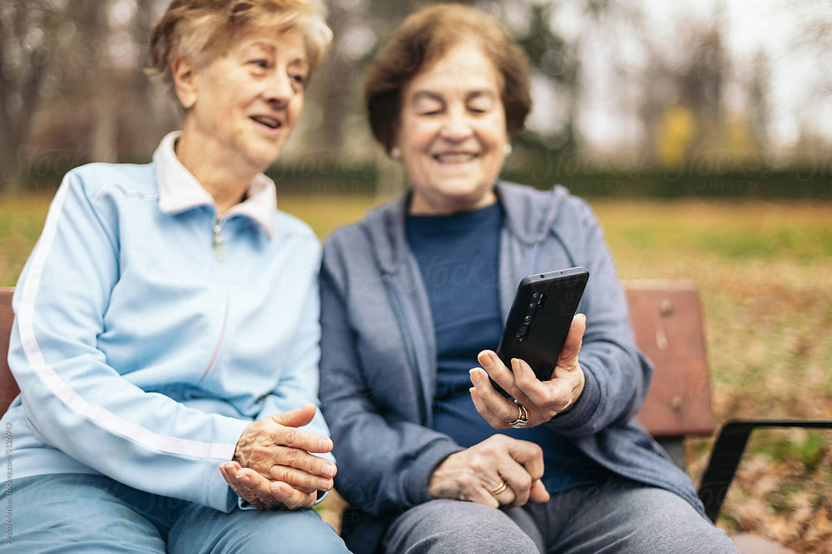 Senior women in sportswear sitting on park bench using smartphone