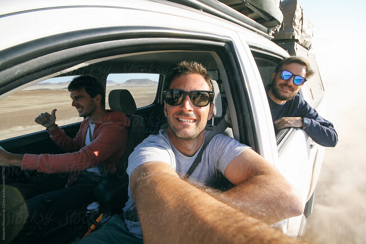 Three young men taking a self portrait through the window of an off-road car during adventure travel