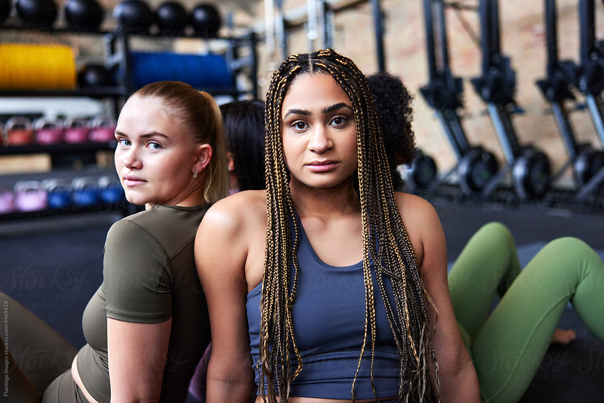 Fit young women sitting back to back in a gym