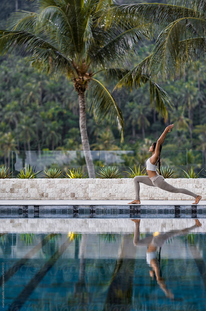 Asian woman practicing yoga on edge of swimming pool in tropical surroundings
