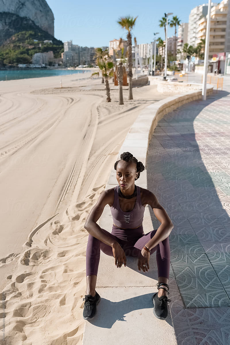 Calm black sportswoman resting on border on beach