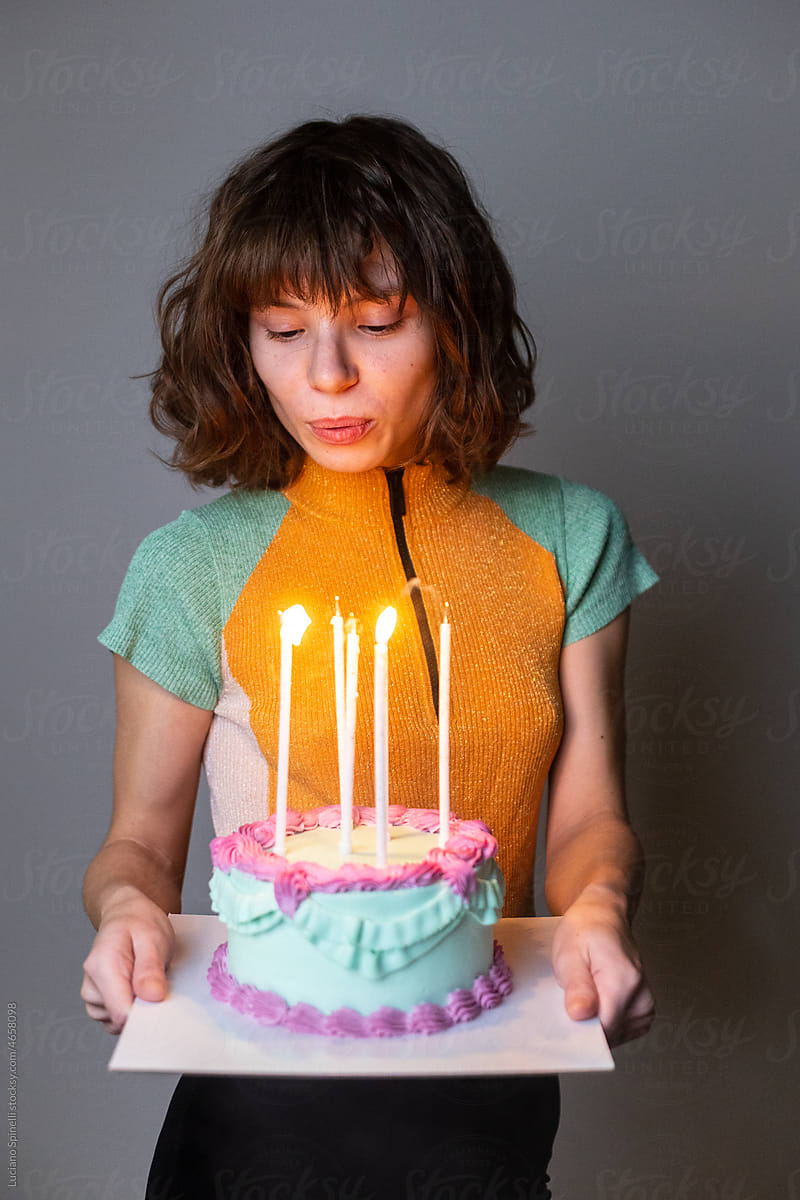 Curly girl blowing out candles on a yummy pastel birthday cake