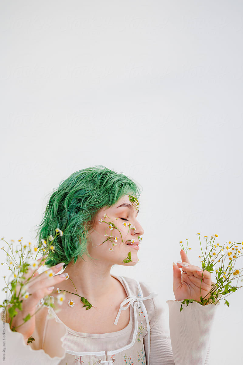 A woman with green hair enjoys the scent of fresh flowers indoors