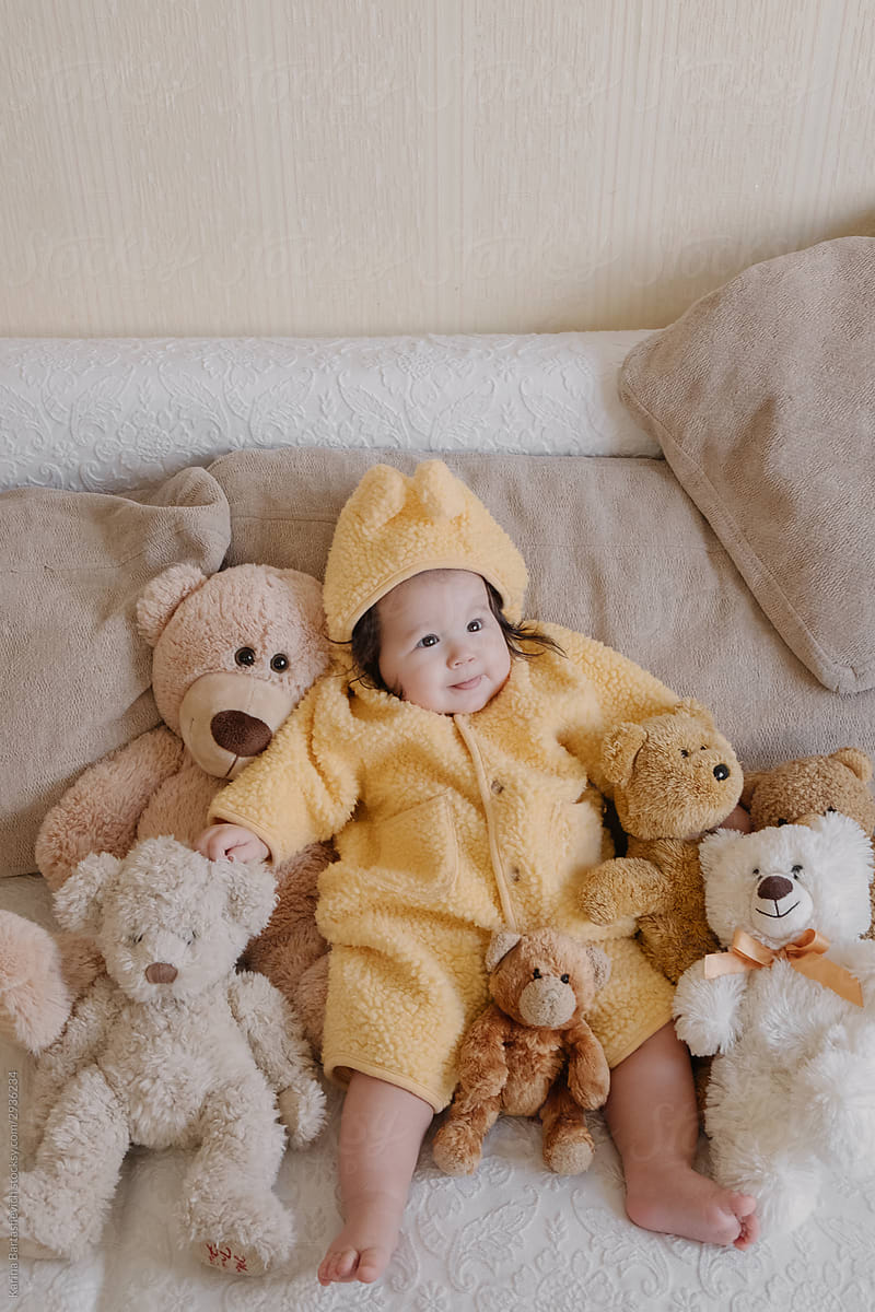 portrait of a baby on a bright sofa surrounded by soft toys and teddy bears