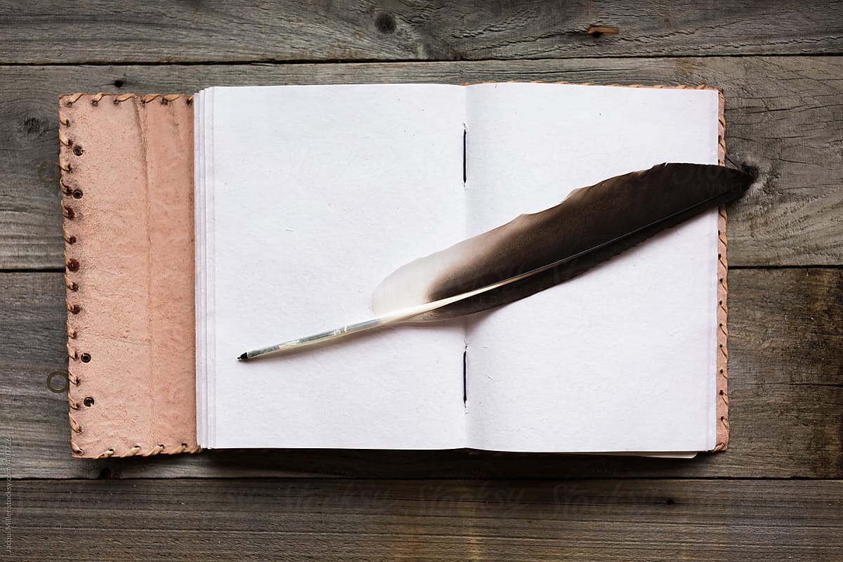 Handmade paper journal with handmade feather quill on rustic wooden table