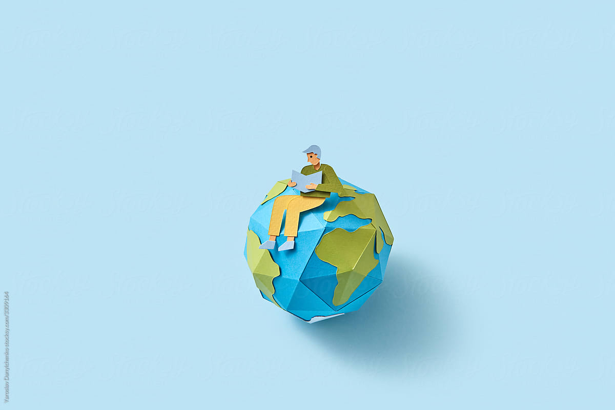 Papercraft man is sitting on a globe and reading.