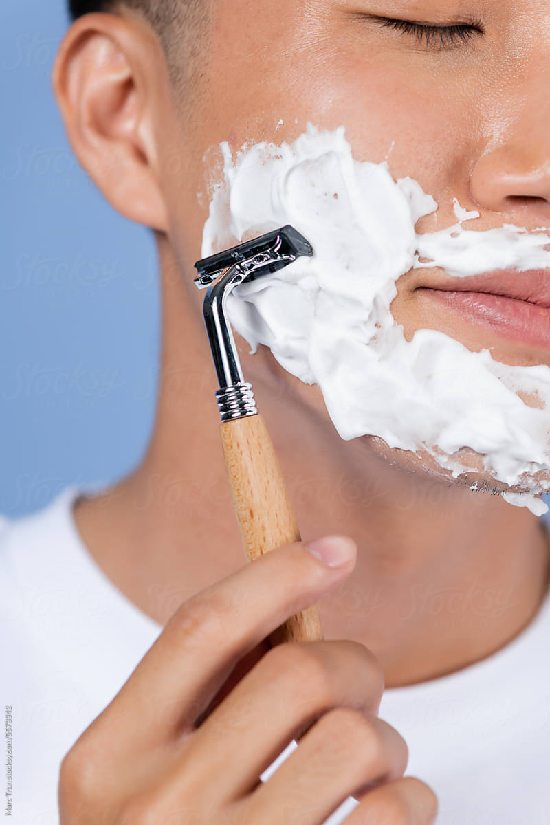 Close up of a handsome young man with reflection shaving