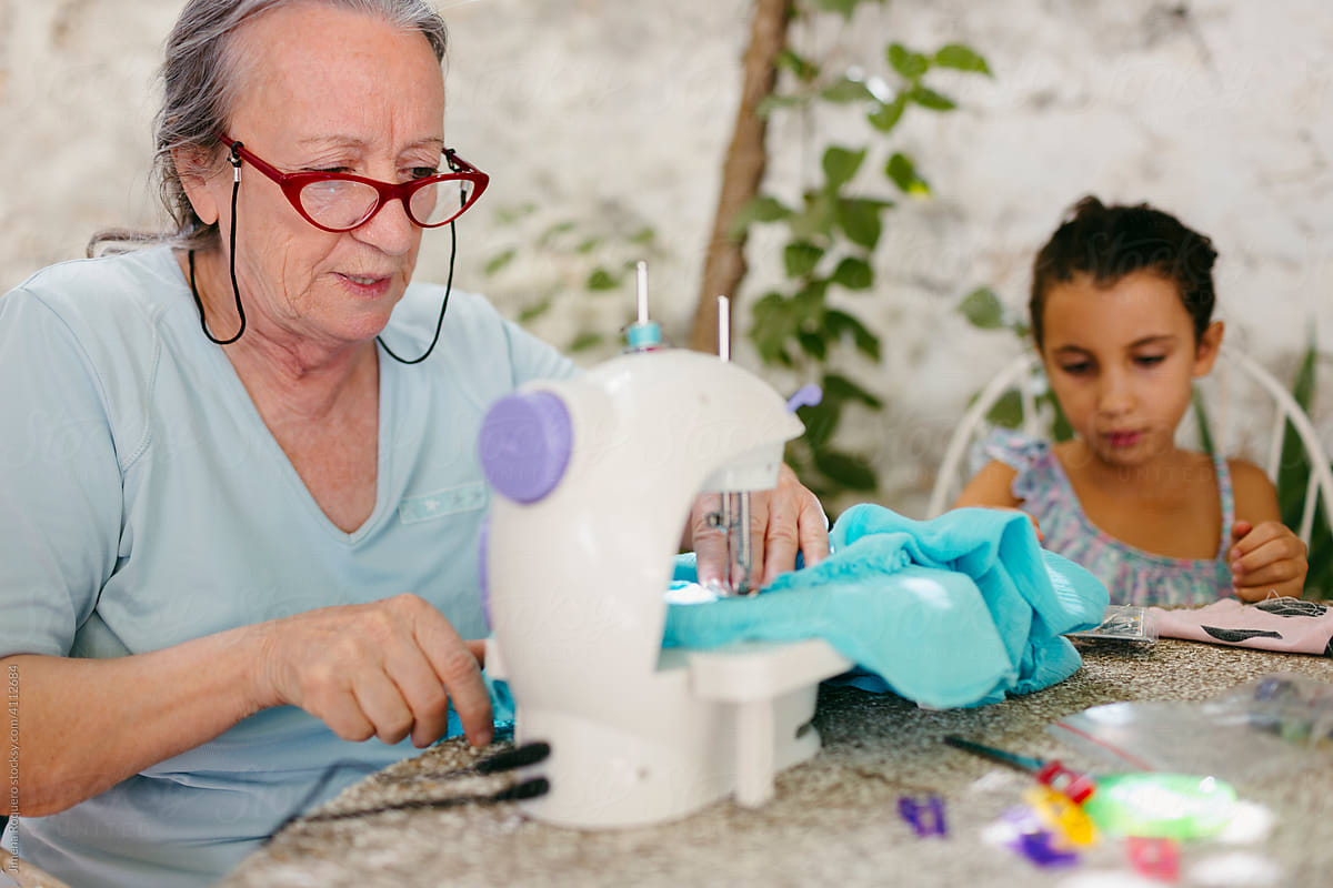 Senior woman using sewing machine next to grandchild
