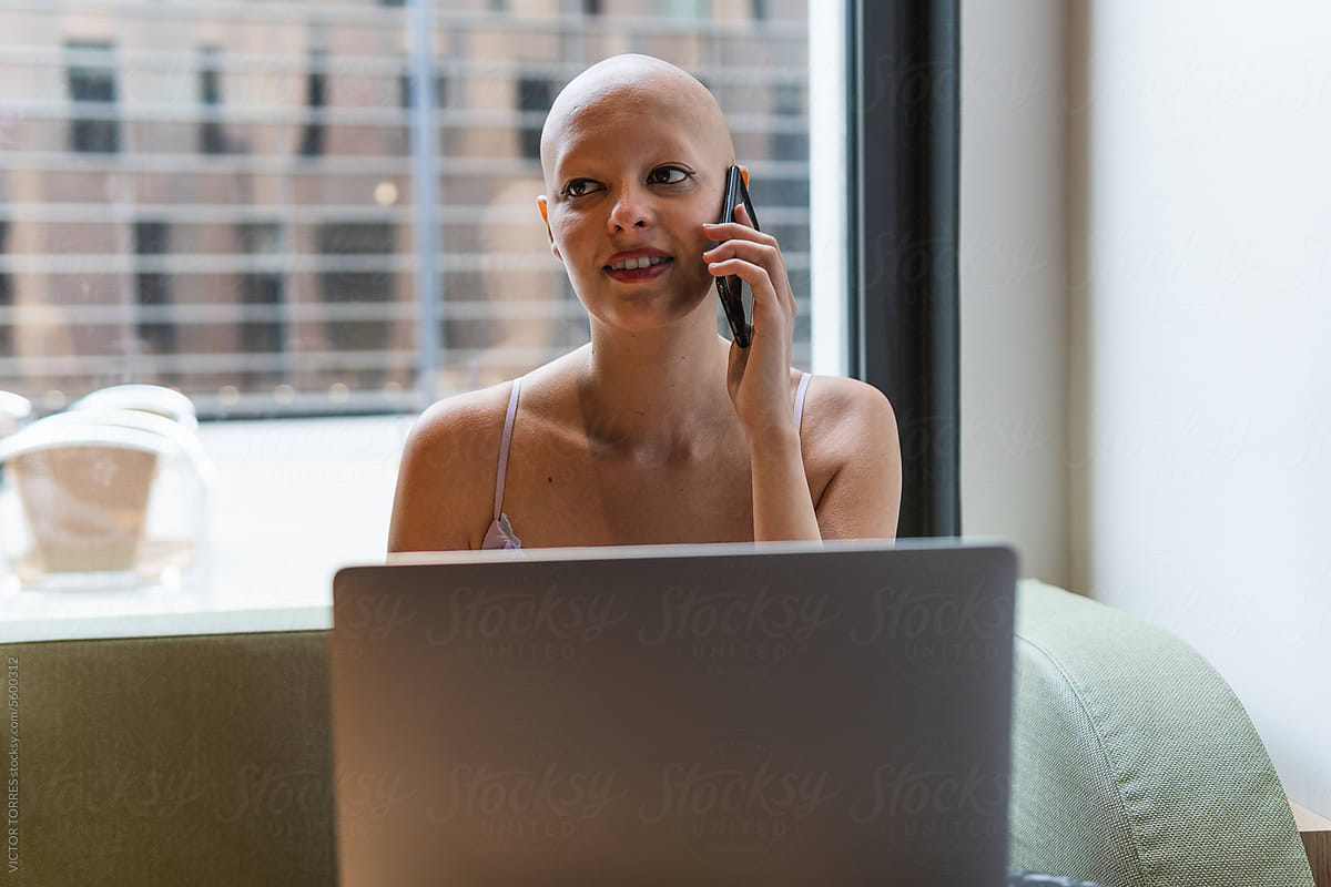 Bald female freelancer speaking on phone while using laptop