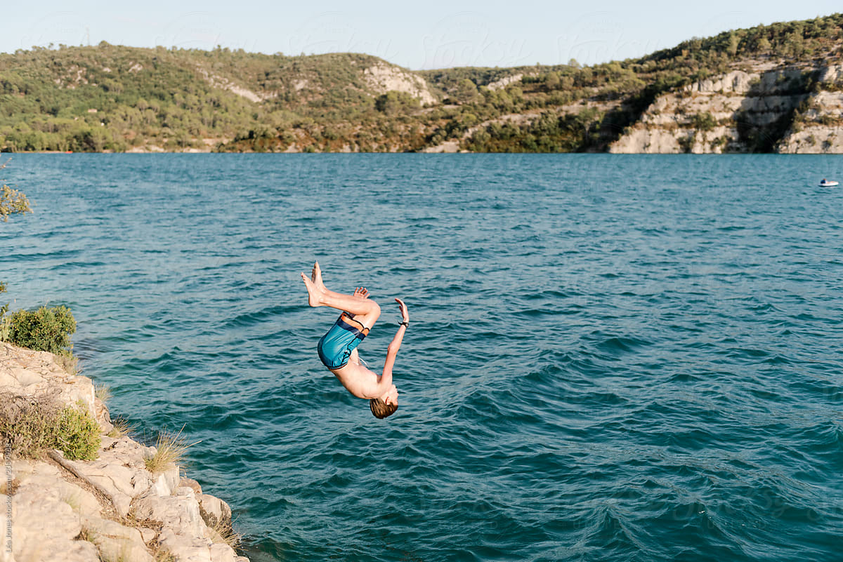 teen boy doing a back flip off a cliff in a lake in Provence