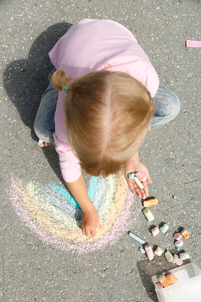 Girl drawing rainbow on sunlit road