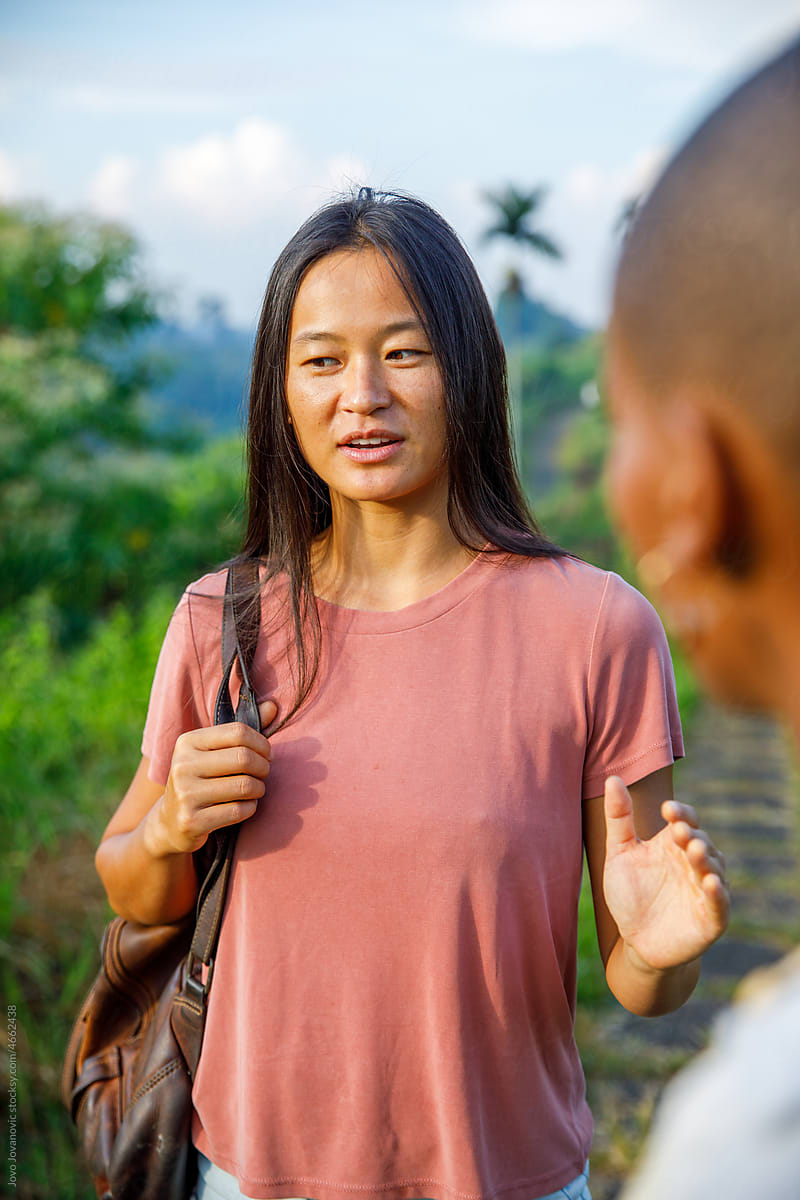 Asian woman talking to friend while holding backpack