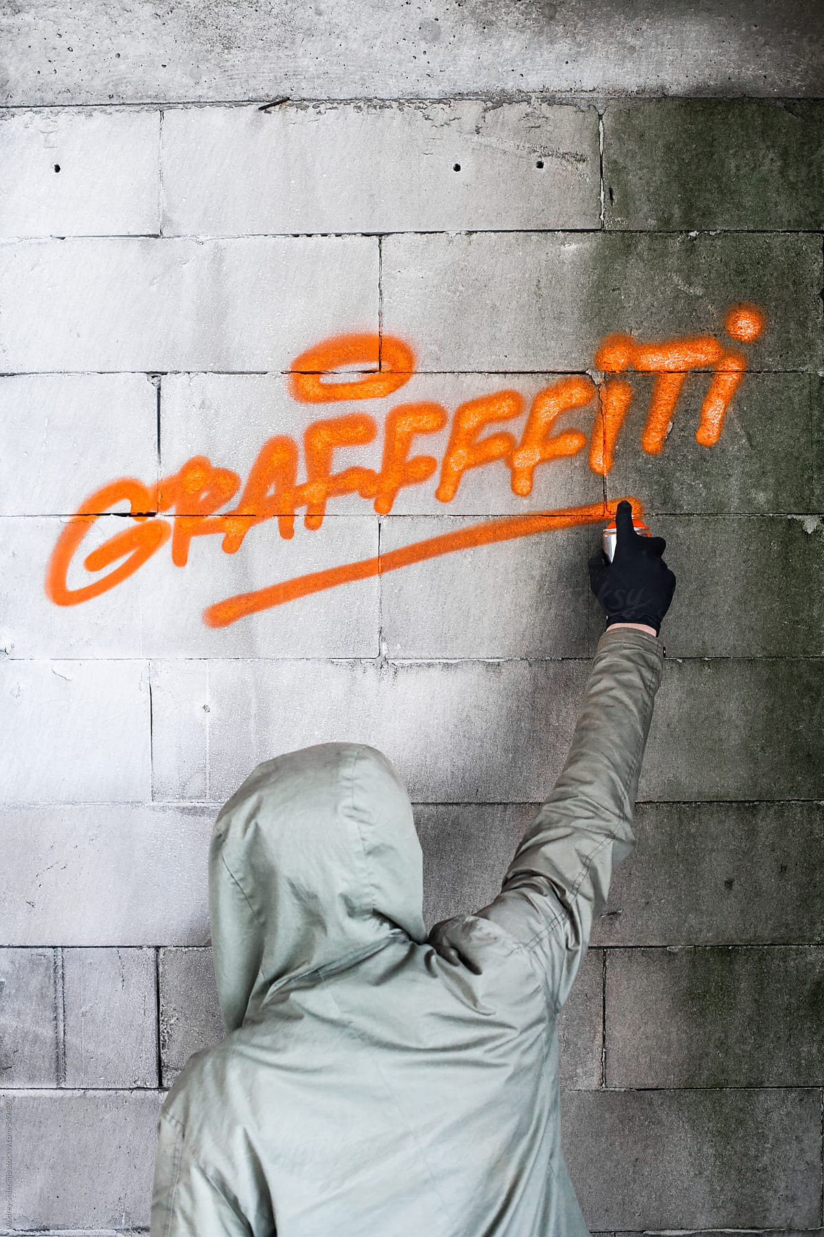 Graffiti artist writing on wall with orange spray.