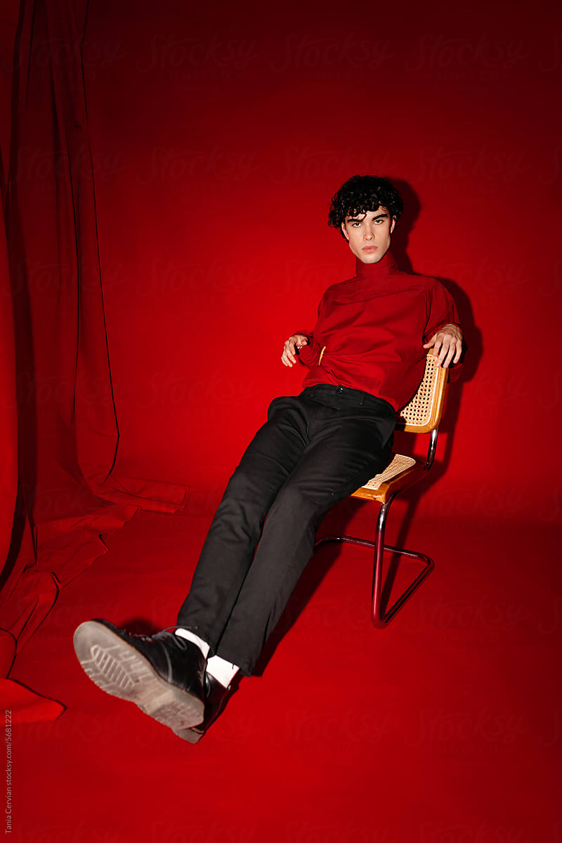 Stylish young man sitting on chair against red backdrop