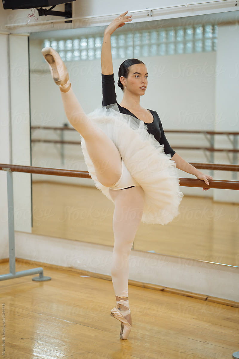 Feminine ballerina performing Arabesque pose near barre