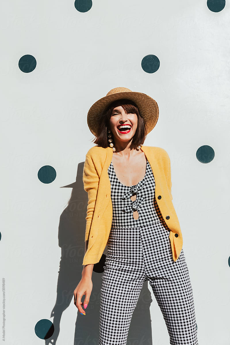 Young stylish woman laughs and poses in front of polka dot wall.