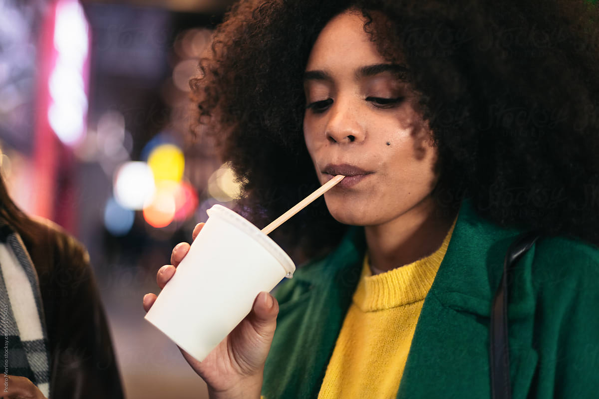 Close-up of afro woman drinking a soda in the city at night
