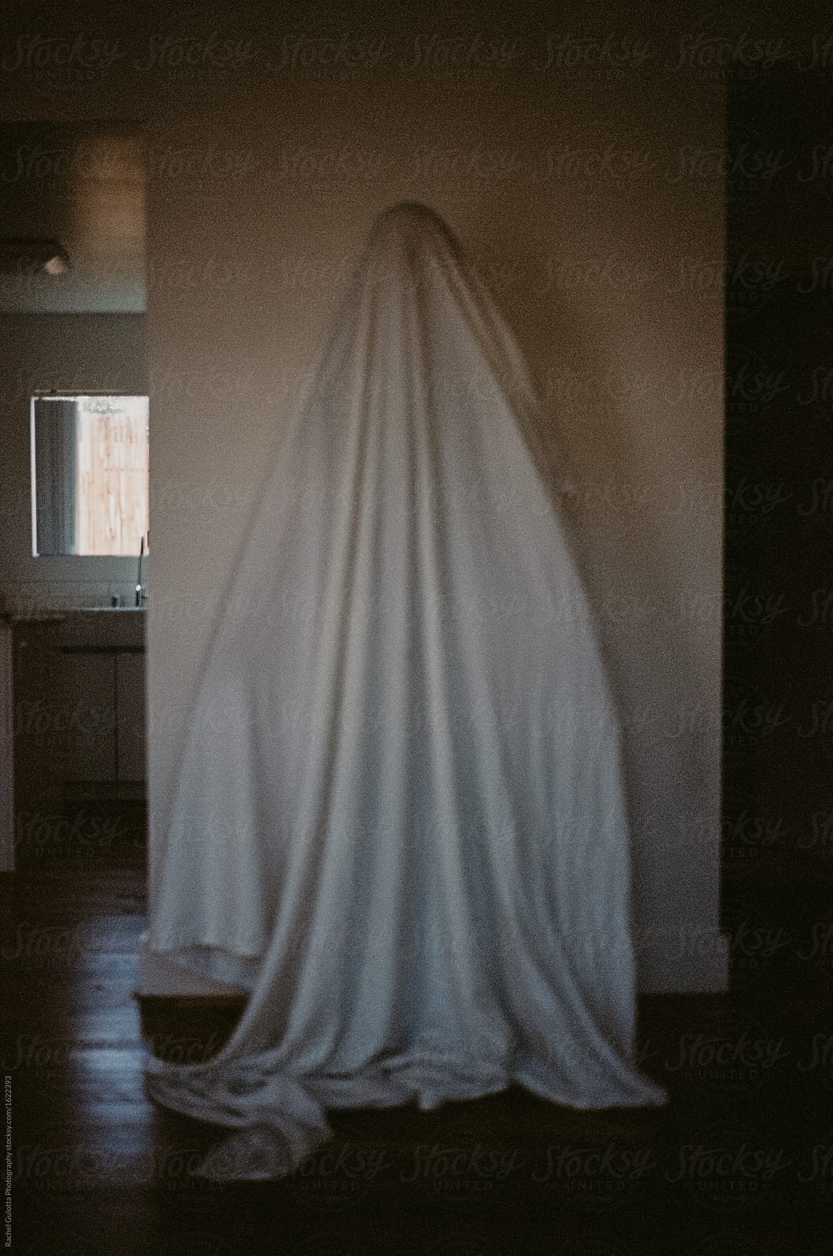 A person with a sheet over head as a ghost costume for halloween in an empty apartment