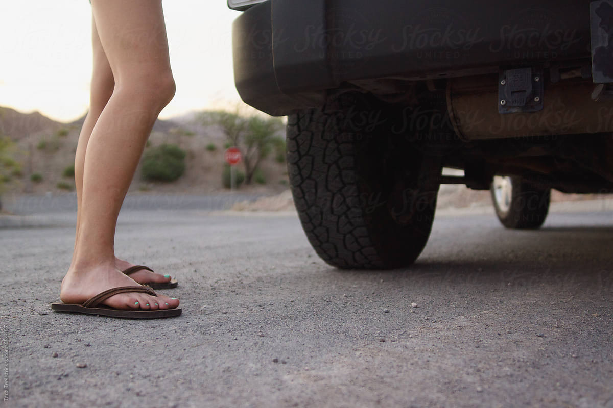 Woman's bare legs in flip flops standing next to vehicle