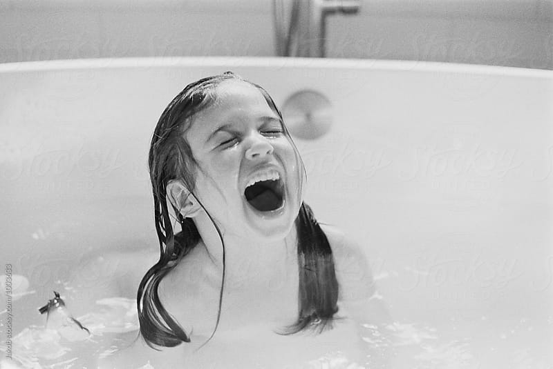 Cute young girl screaming of joy in a bath tub
