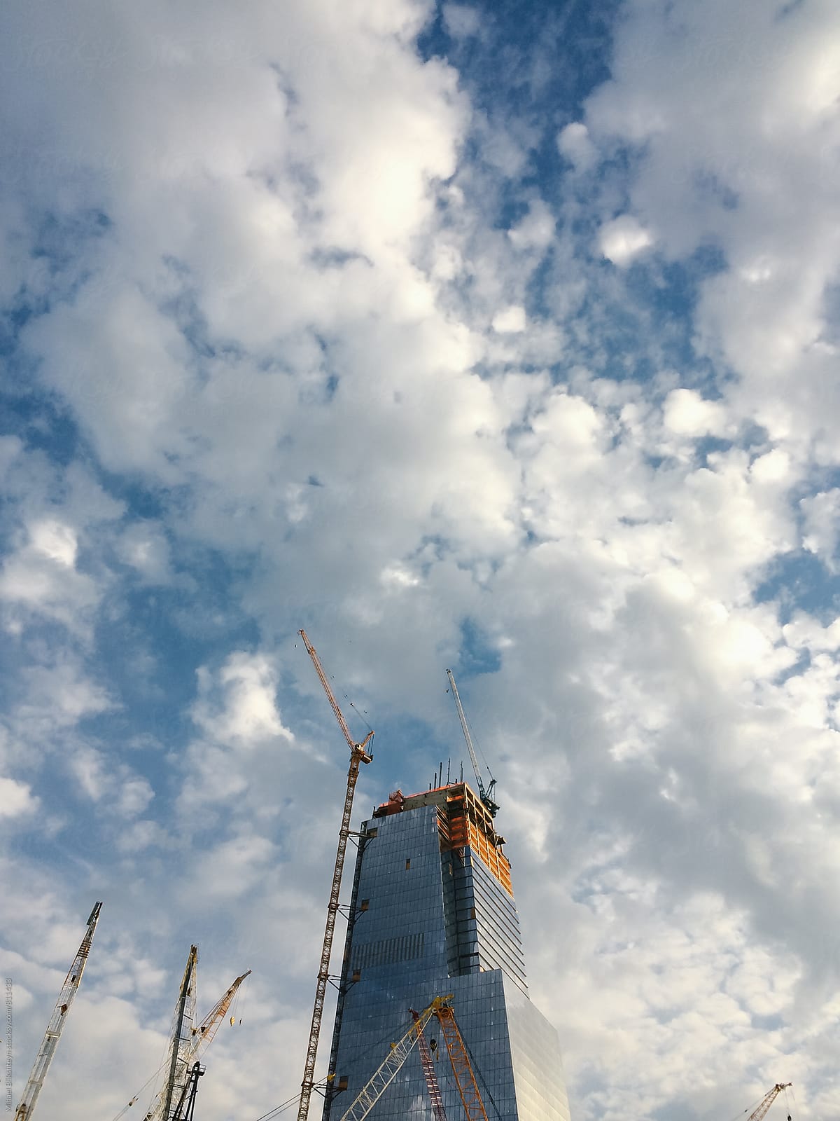 Construction of a skyscraper in a city with cranes against blue sky with clouds