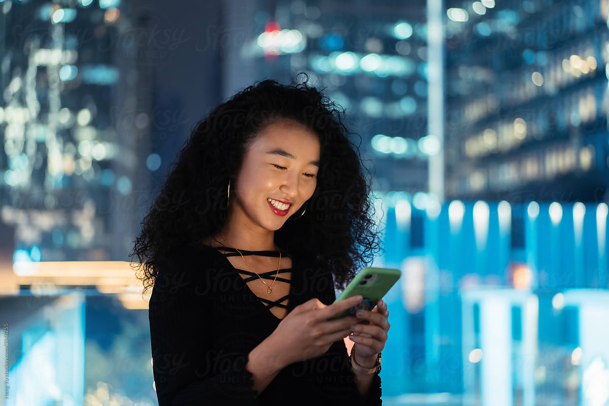 Woman playing phone in front of the night cityscape