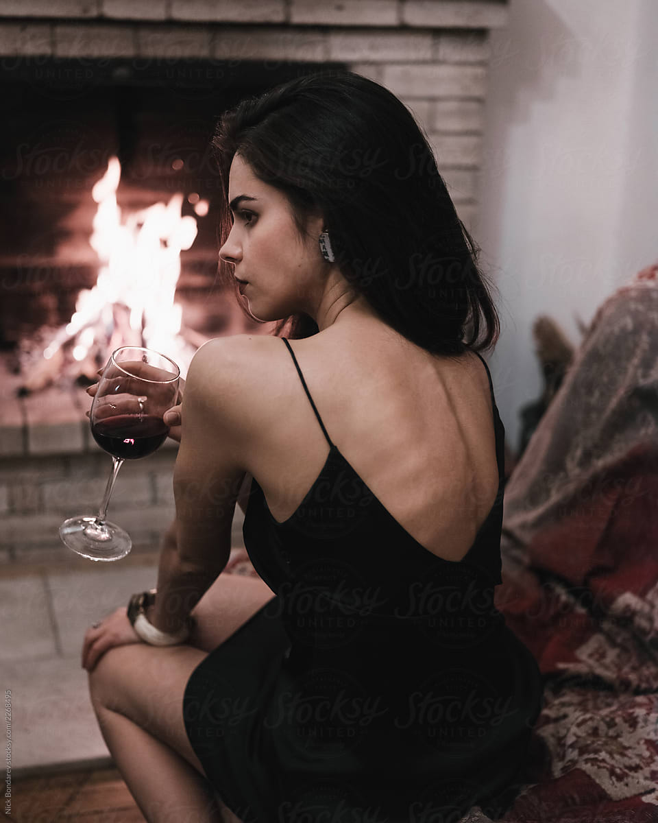 Woman In A Black Dress In Front Of Fireplace With Glass Of