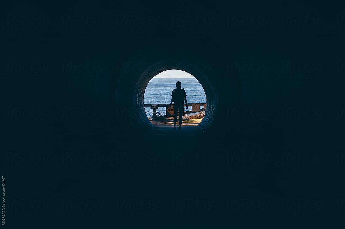 Silohuette of a woman wearing a backpack in a tunnel looking out to sea.