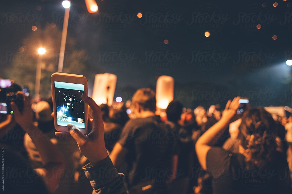 People taking photos on phone of lanterns in night sky