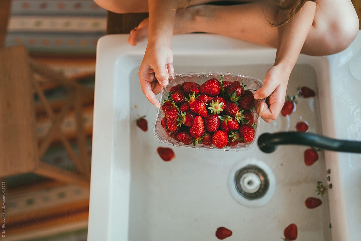 Girl washing a basket with strawberry.