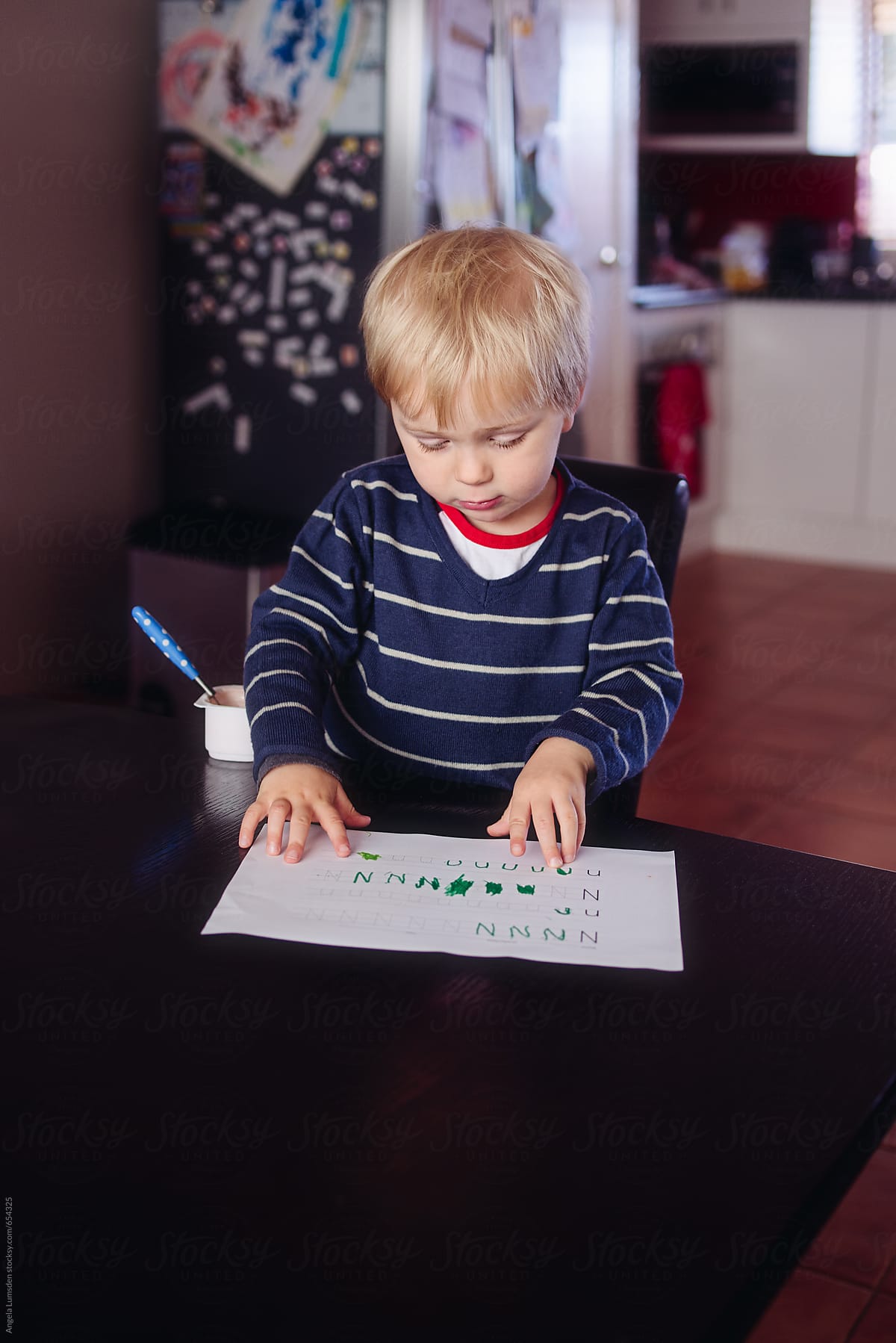 Small boy sitting at a table proudly showing off a sheet of handwritten letters