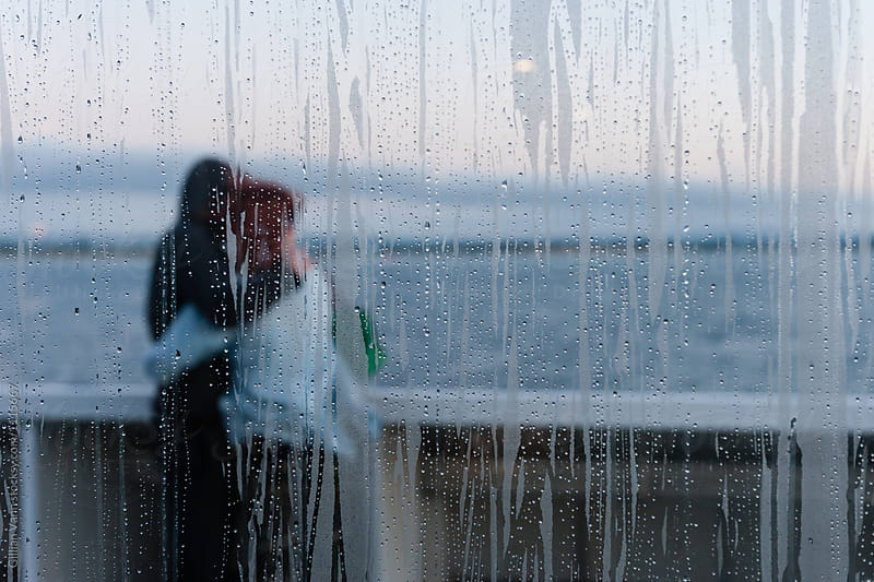 water droplets on a window with blurry couple stading outside in