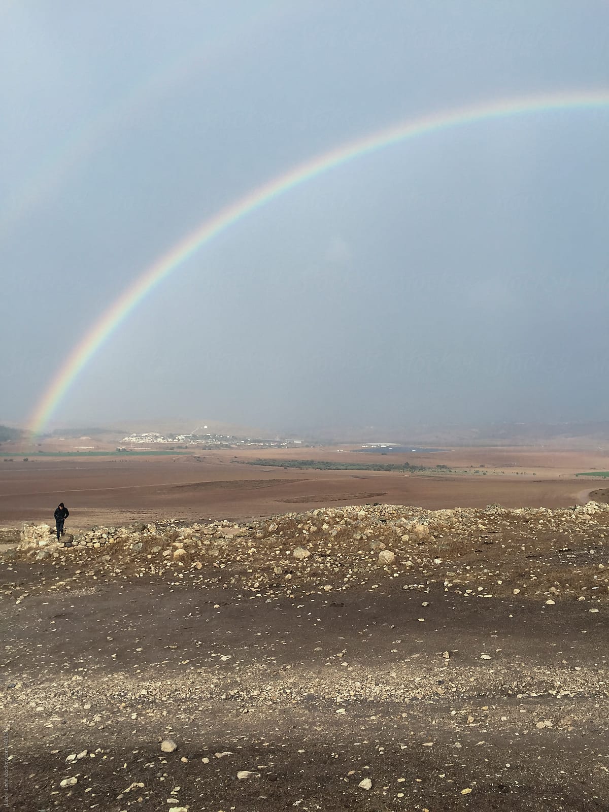 Man walking away from rainbow in a rural biblical landscape