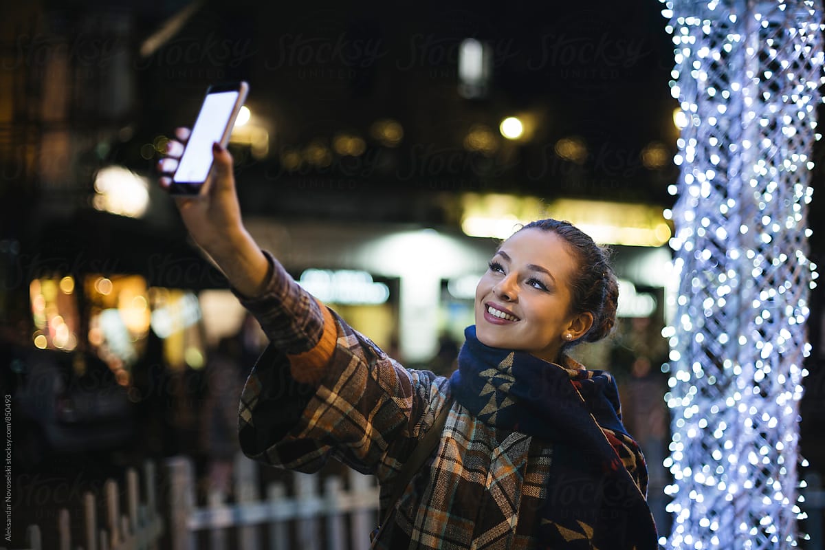 Beautiful woman taking a selfie in urban environment, by night