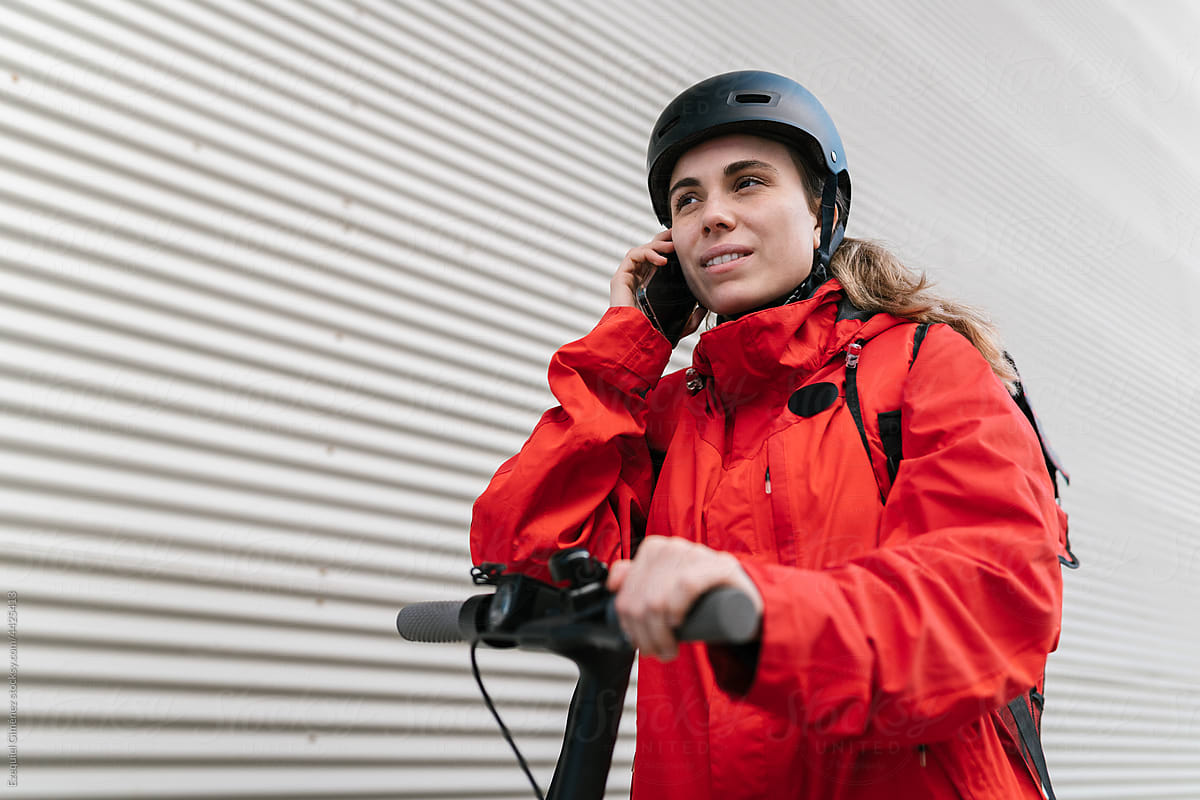 Female courier answering smartphone call on e scooter